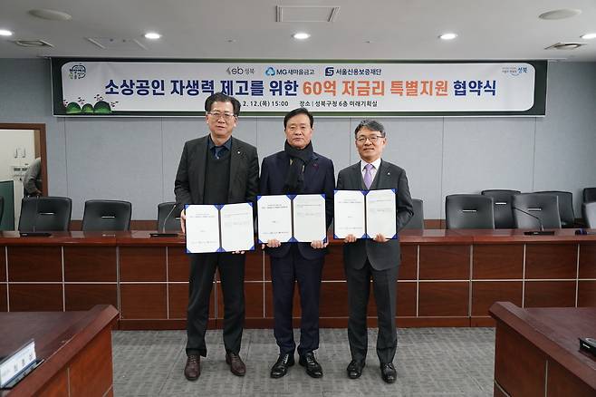 이승로 성북구청장을 포함한 세 명의 남성이 실내에서 협약서로 보이는 서류를 들고 서 있는 사진이다. 배경에는 ‘소상공인 자생력 제고를 위한 60억 저금리 특별지원 협약식’이라고 적힌 현수막이 걸려 있다.