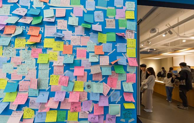 빼곡히 붙어있는 포스트잇 뒤로 전시장을 둘러보는 관람객들이 보인다. /김지호 기자