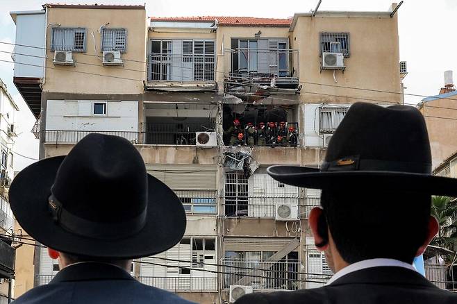 15일(현지시각) 이스라엘 텔아비브 동부 브네이브락에 있는 아파트가 요격된 이란의 미사일 잔해로 일부 파괴된 모습을 이스라엘의 초정통파 유대교인들이 지켜보고 있다. AFP 연합뉴스