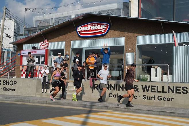 해양레저 브랜드 서프홀릭이 부산 송정 해변가 본점 매장 전면에 'SongJeong Runner's Station' 사인물을 설치한 두 러너를 위한 커뮤니티 거점 공간 운영을 시작해 주목받고 있다. 사진=BRC크루 승훈 작가 제공
