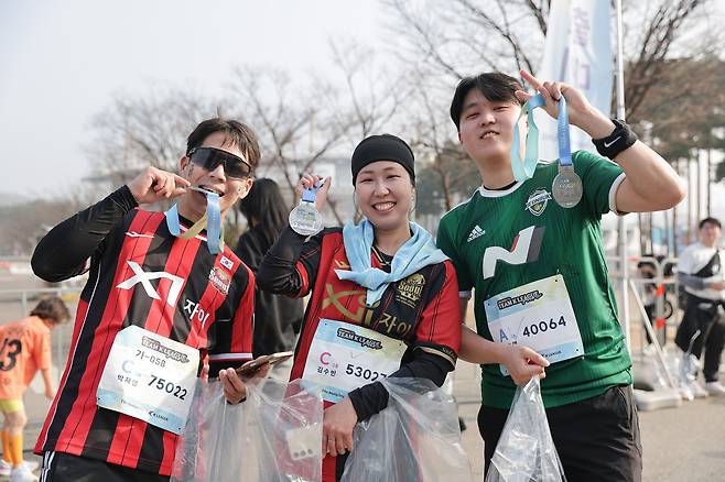 서울 상암동 월드컵공원 평화광장 일대에서 열린 2026 서울 팀 K리그 행사에서 10km를 완주한 뒤 기념 메달을 함께 들어 보이며 포즈를 취한 서울과 전북의 축구 팬. 사진 프로축구연맹