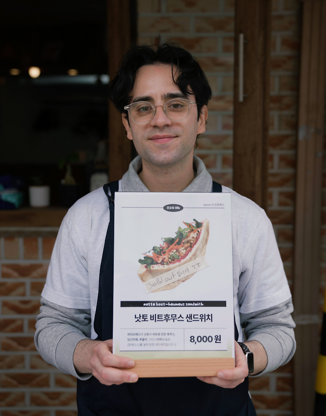 Minjun Cooks holds a sign promoting his beet hummus natto sandwich, which sold out at a natto event in Seoul. (Tammy Park/The Korea Herald)