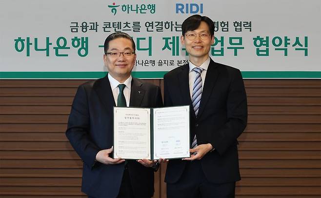 이호성 하나은행장(왼쪽)과 배기식 리디 대표이사가 지난 10일 서울 을지로 하나은행 본점에서 업무협약서를 들고 기념촬영을 하고 있다. 이번 협약은 양사가 금융·콘텐츠를 결합해 손님에게 새로운 경험 제공하기 위해 마련됐다. 하나은행 제공