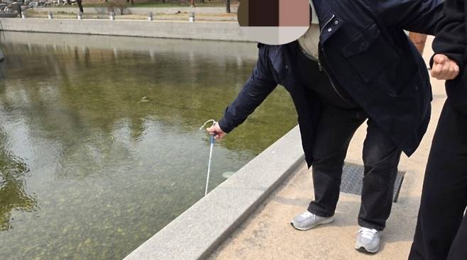 ▲ 지난달 27일 오후 인천 중구 월미공원을 찾은 시각장애인 A씨가 연못에 지팡이를 넣어 수심을 확인하고 있다. /곽안나 기자 lucete237@incheonilbo.com