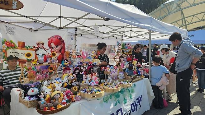 ▲ 고모저수지 인근 광장에서 열린 '고모마켓' 부스를 찾은 관광객들이 수공예품을 둘러보고 있다. 상인과 주민들이 직접 운영하는 이러한 체험형 콘텐츠는 고모리만의 독특한 문화 상권을 형성하는 밑거름이 됐다. /이광덕 기자 kdlee@incheonilbo.com