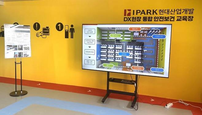 충남 '천안 아이파크 시티 5·6단지' 건설 현장에 구축된 'DX현장 통합 안전보건 교육장' 모습. 대형 모니터와 벽면 픽토그램을 통해 근로자가 신규 등록부터 혈압 측정, 안전 교육, 보건 면담까지 담당자 안내 없이 스스로 진행할 수 있도록 이동 동선을 직관적으로 안내하고 있다. IPARK현대산업개발