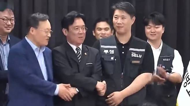 김영훈 장관(가운데)이 지난 20일 경기고용노동청에서 열린 삼성전자 임금협상 조정회의에서 노사 관계자들과 손을 맞잡고 있는 모습. 김 장관은 최근 대기업 초과이익의 사회적 분배 필요성을 언급했다. (SBS 캡처)