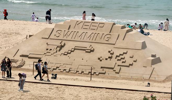 9일 부산 해운대해수욕장을 찾은 관광객들이 방탄소년단(BTS) 신곡 'KEEP SWIMMING'이 적힌 대형 모래 작품을 구경하고 있다. 2026.6.9 / 사진=연합뉴스