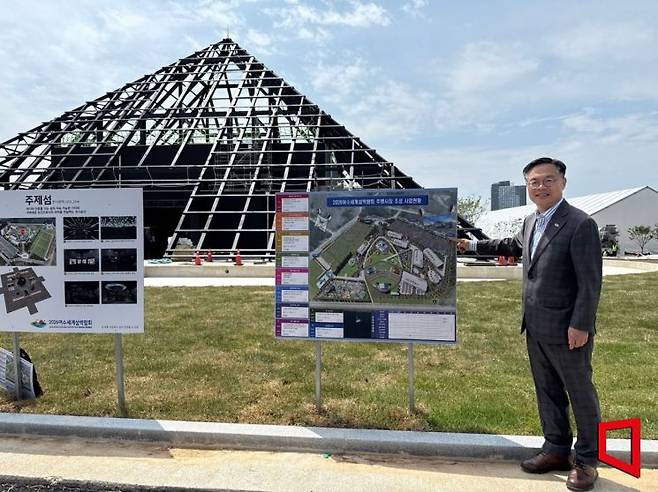 김종기 2026여수세계섬박람회 조직위원회 사무총장이 9일 전남 여수 돌산 진모지구 주행사장에서 조성 현황을 설명하고 있다. 뒤편에는 박람회 랜드마크인 피라미드형 주제관 ‘주제섬’이 공사 중이다. 김희윤 기자