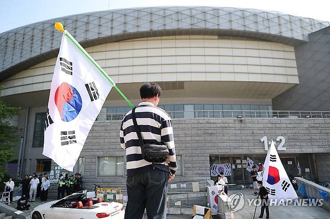 지속되는 개표소 봉쇄 시위 (서울=연합뉴스) 김성민 기자 = 6·3 지방선거 투표용지 부족 사태로 빚어진 '잠실 개표소 봉쇄 시위'가 이어지고 있는 11일 서울 송파구 올림픽공원 핸드볼경기장에서 한 참가자가 태극기를 들고 있다. 2026.6.11 ksm7976@yna.co.kr