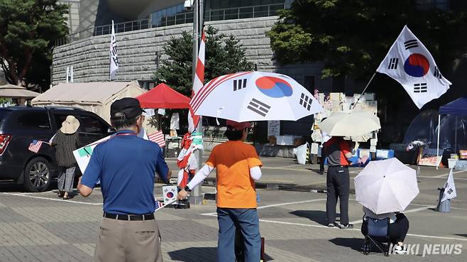 26일 서울 올림픽공원 핸드볼경기장 앞 한 시위 참가자가 성조기와 태극기가 합성된 우산을 들고 핸드볼경기장 앞을 걷고 있다. 유정민 기자