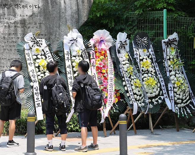 1일 서울 강동구 배재고 앞에 근조 화환이 놓여 있고 그 앞을 지나가던 학생들이 문구를 읽어보고 있다. 연합뉴스