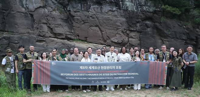Participants in the 8th World Heritage Site Managers' Forum, including Korea Heritage Service Administrator Huh Min, seventh from right in the front row, and Ulsan Mayor Kim Sang-woo, sixth from right in the front row, pose for a photo in front of the Unesco-listed petroglyphs along the Bangu Stream on July 17. NEWS1