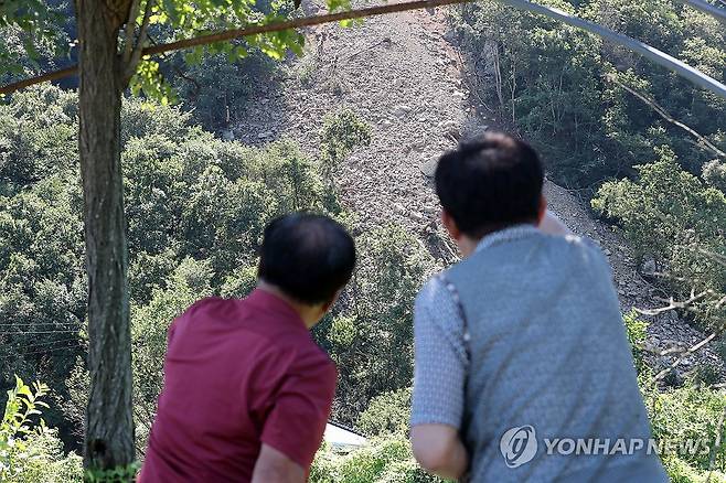 '저기서 무너져 내렸어요' (홍천=연합뉴스) 강태현 기자 = 4일 오전 강원 홍천군 서면 모곡리에서 산사태가 발생해 비탈면이 무너지면서 암석과 토사가 흘러내리고 있다.
인명피해나 민가 피해는 없었으나 산사태로 농기계를 보관하는 창고 1동이 매몰됐다. 사진은 마을 주민들이 산사태 현장을 바라보는 모습. 2026.9.4 taetae@yna.co.kr